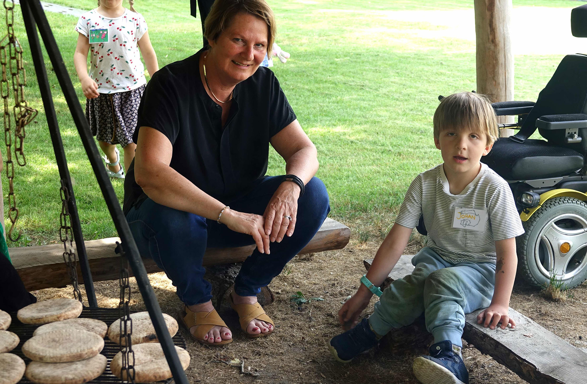 Centerbørnehavens leder sidder ved bålplads sammen med dreng med cerebral parese